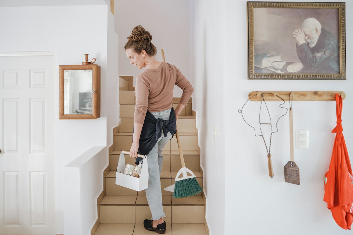 House cleaner carrying a supply caddy and broom up the stairs of a home